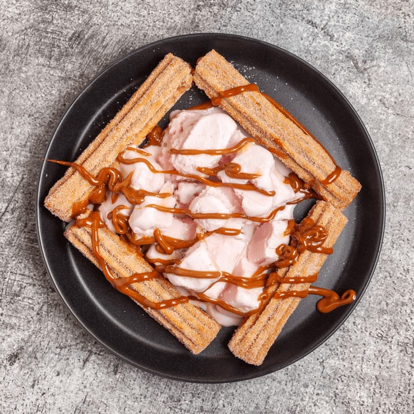 Churros with pink ice cream and caramel drizzle on a black plate at Luis Mexican Food & Grill.