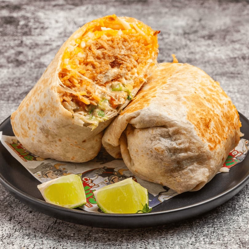 Two large, golden-brown burritos, one cut open to reveal a savory filling, served with lime wedges.