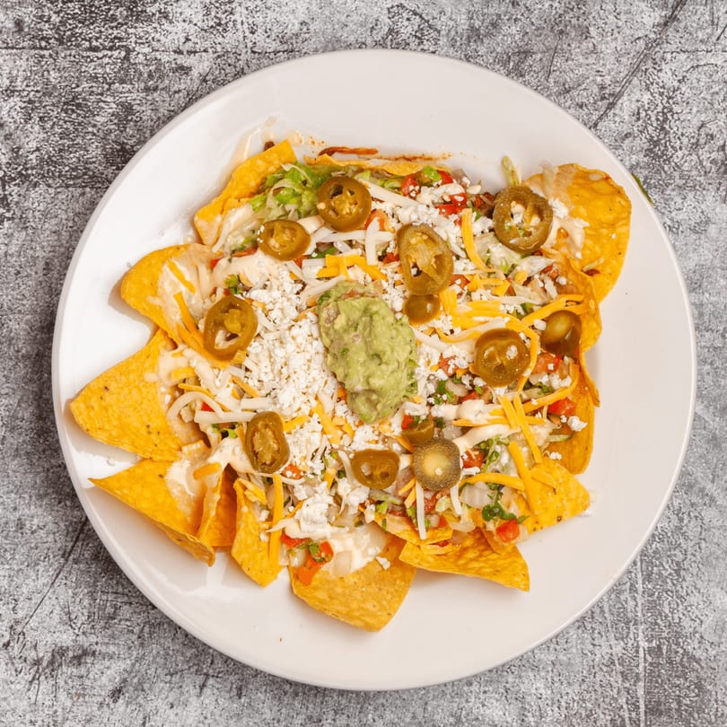 Luis Mexican Food & Grill nachos with cheese, jalapenos, and guacamole on a white plate.