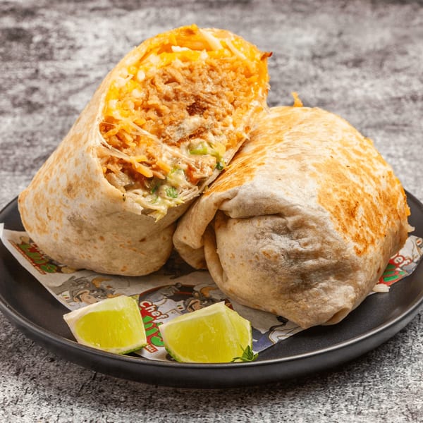 Two large, golden-brown burritos, one cut open to reveal a savory filling, served with lime wedges.