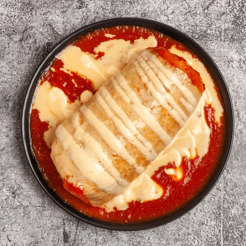 Luis Mexican Food & Grill's burrito covered in red sauce and cheese, served in a black bowl.