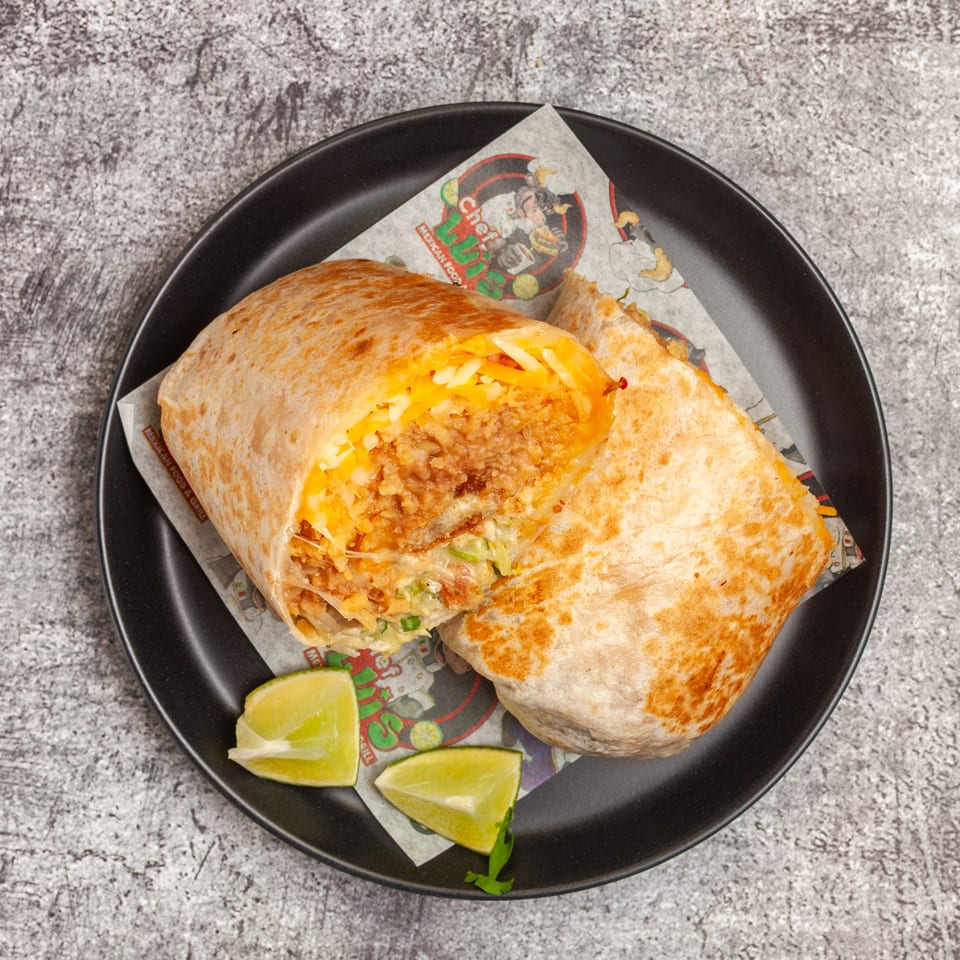 A large, cut Luis Mexican Food & Grill burrito with cheese and meat, served with lime wedges.