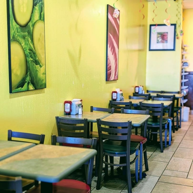 Bright yellow walls and tiled floors in a casual dining area with multiple tables and chairs.